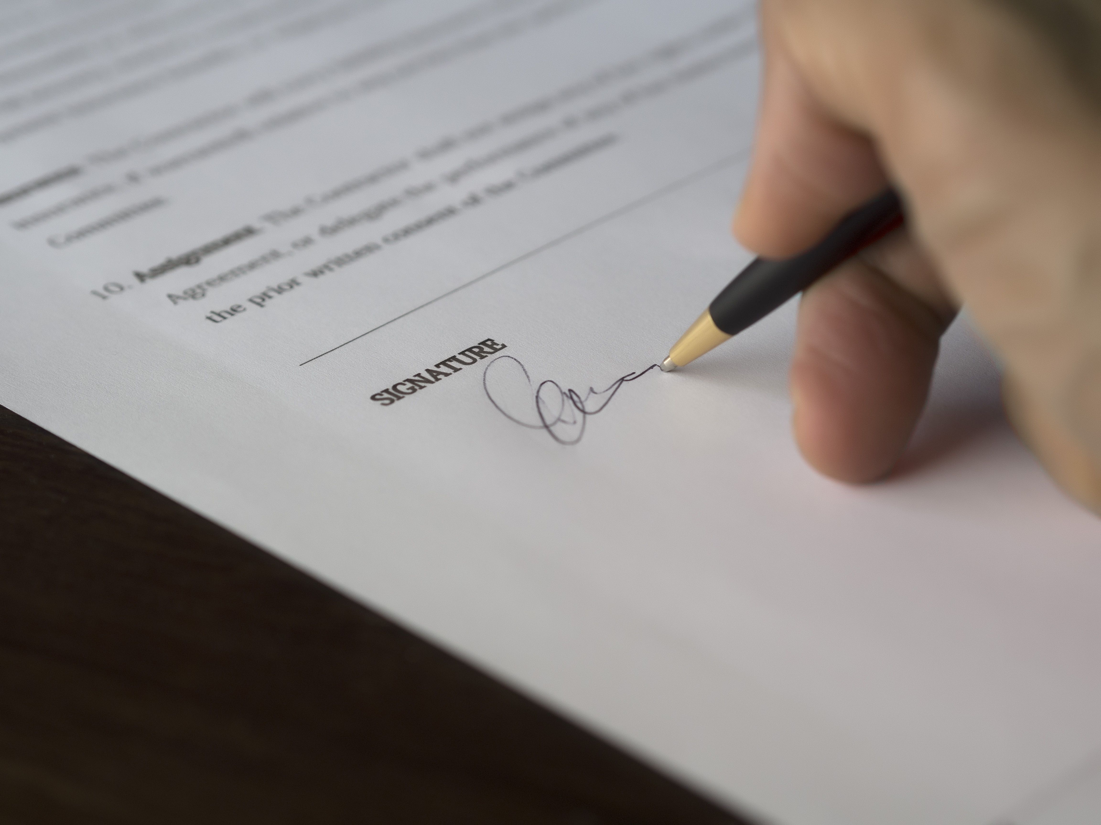 Close-up of a hand signing a formal contract on a wooden desk